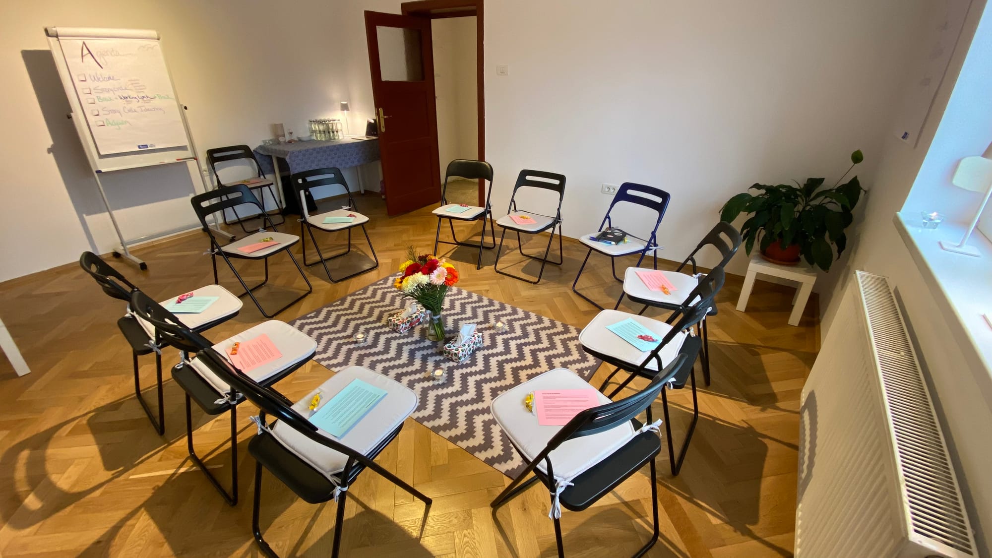 A circle of chairs arranged in a room, with flowers in the middle.